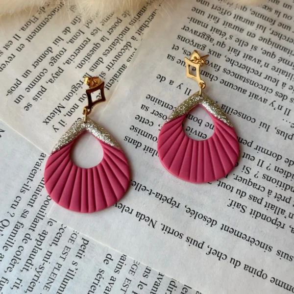 boucles d'oreilles "lucienne" de couleur rose posées sur des pages d'une livre