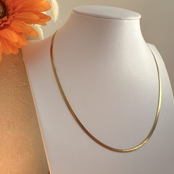 Collier Léonie, fin et doré posé sur un buste, Fleur orange en arrière plan