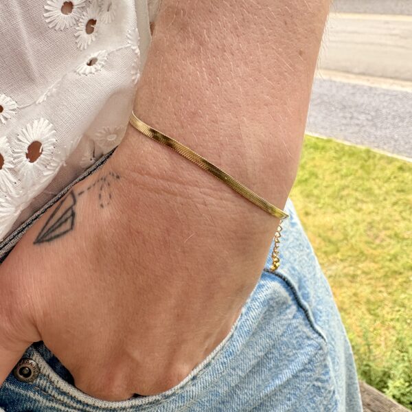 Bracelet fin maille plate en acier inoxydable doré porté au poignet